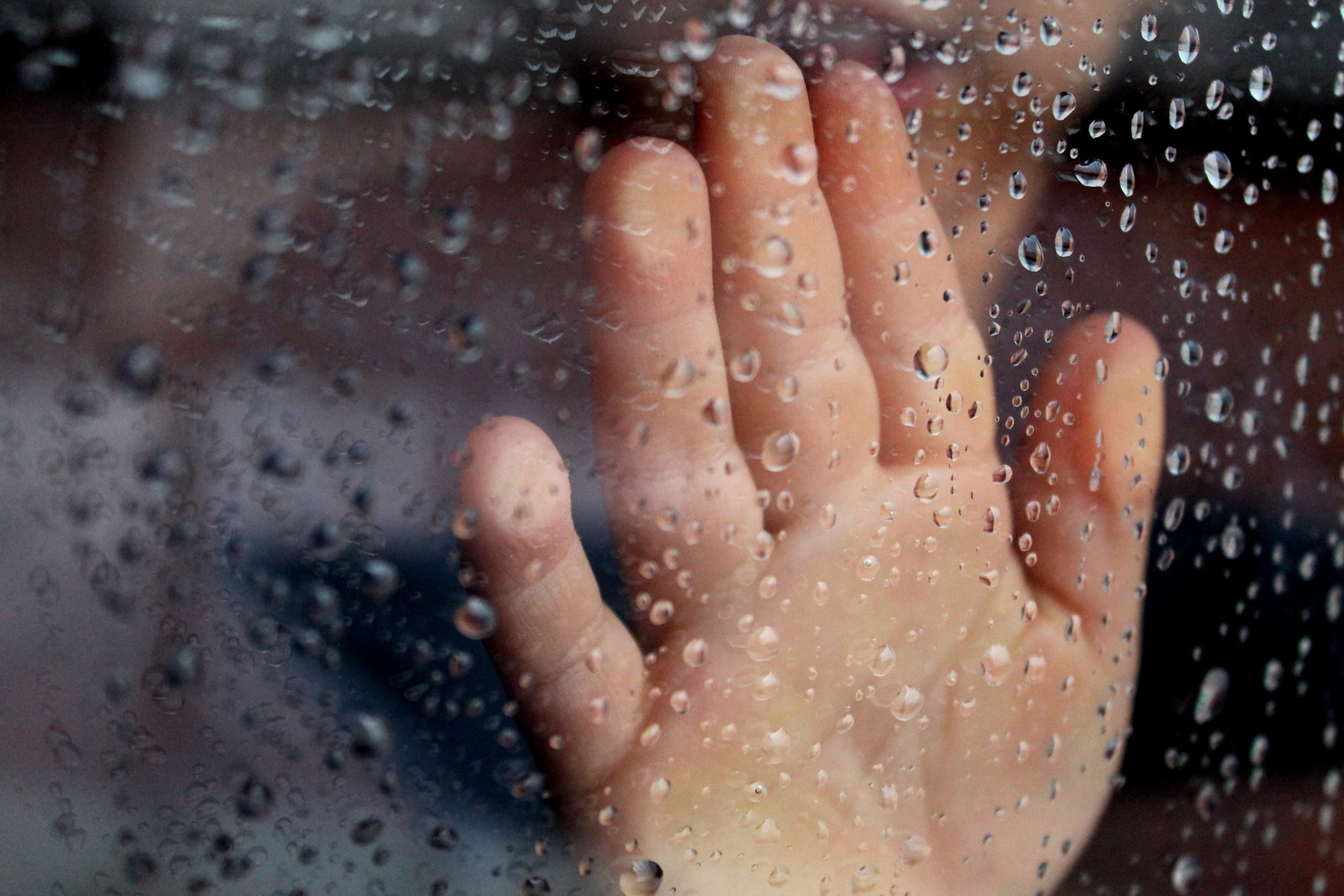Mão de criança na janela durante a chuva. Imagem ilustrativa texto brincadeiras para os dias de chuva.