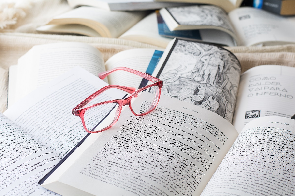 Óculos de armação vermelha sobre livros. Imagem ilustrativa texto leituras profundas.
