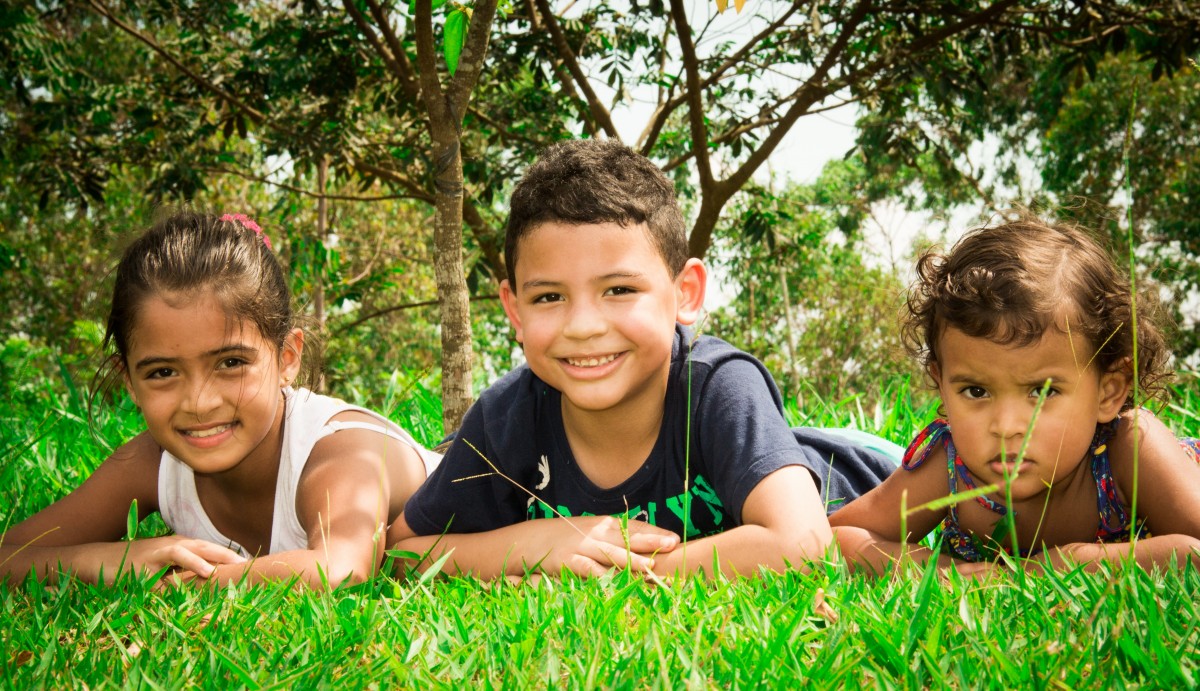 Três crianças na grama. Imagem ilustrativa texto férias escolares.