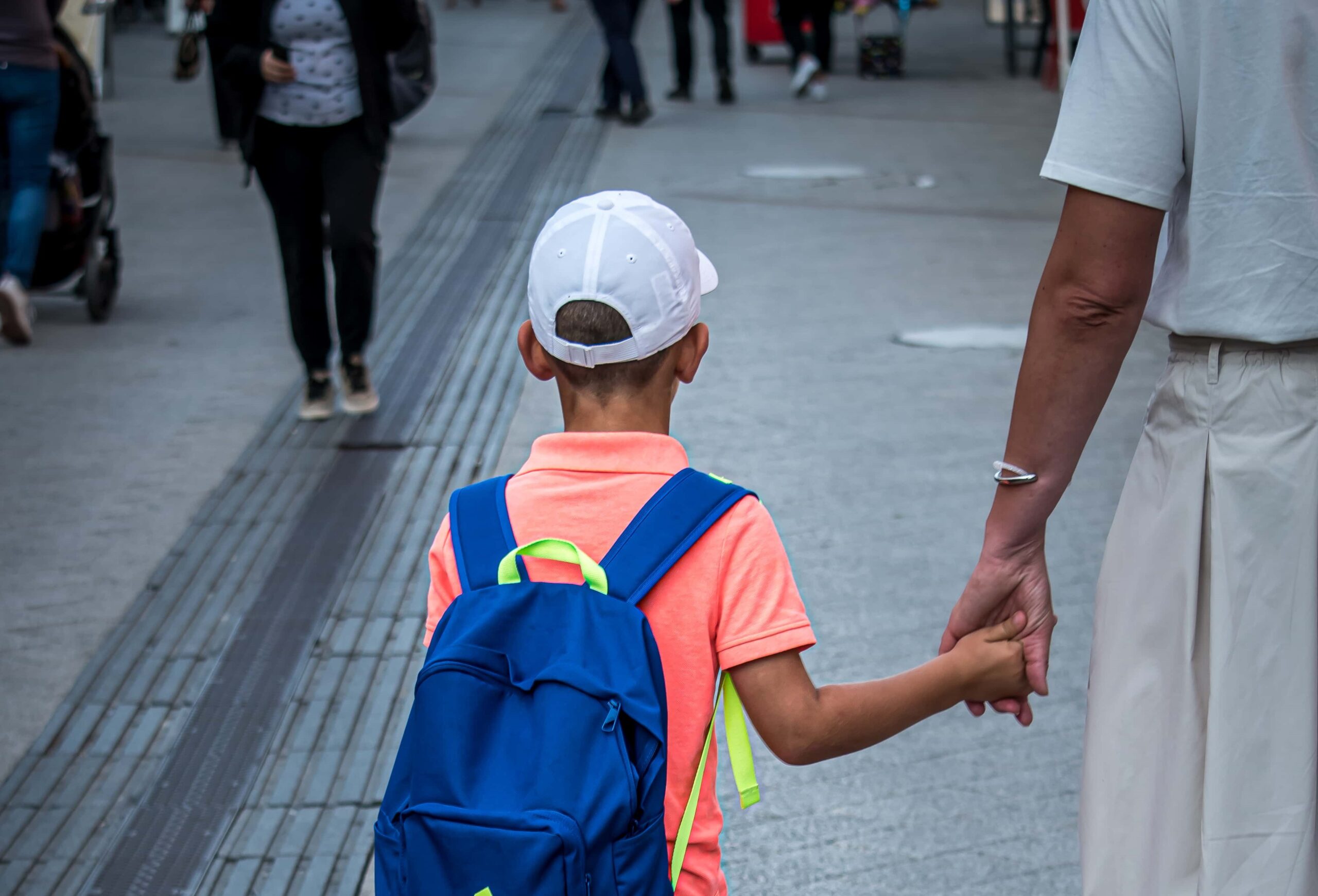 Mãe dando mão ao filho, andando na rua. Imagem ilustrativa texto evasão escolar.