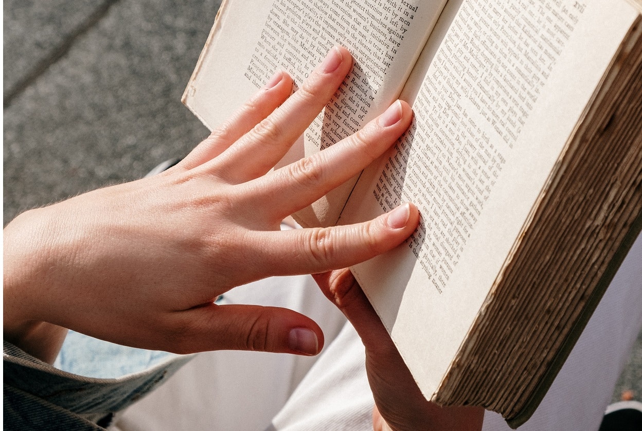 Mão de mulher sobre livro aberto, ao ar livre. Imagem ilustrativa texto técnicas de leitura.