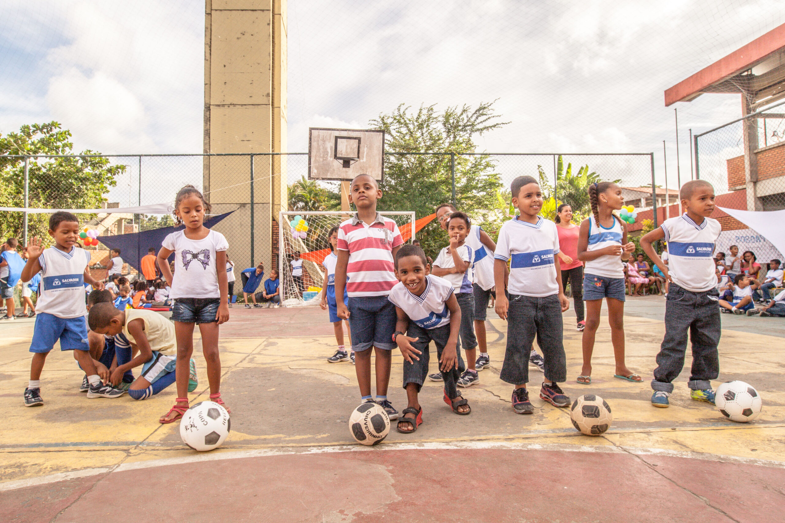 Meninos e meninas com bolas de futebol na quadra da escola. Imagem ilustrativa texto Dia das Mulheres na escola.