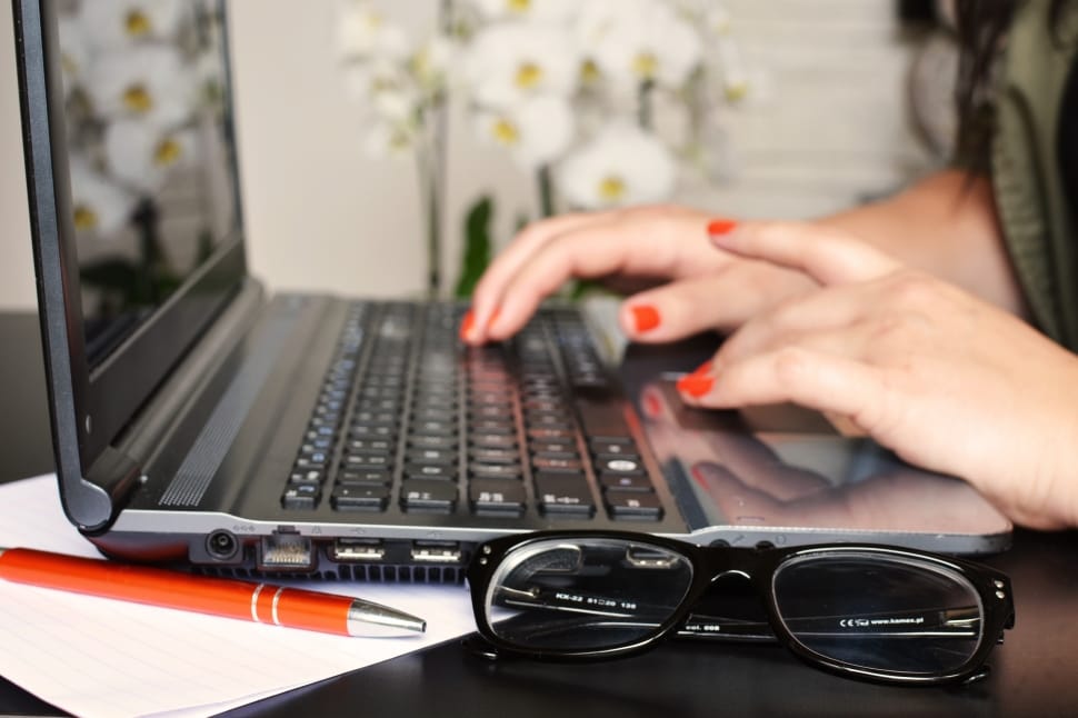 Mão de mulher digitando no computador, com óculos e caneta do lado. Imagem ilustrativa texto conhecer autor.