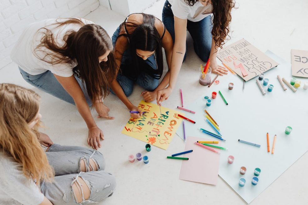 Meninas escrevendo cartazes coloridos no chão. Imagem ilustrativa texto inteligência artificial.