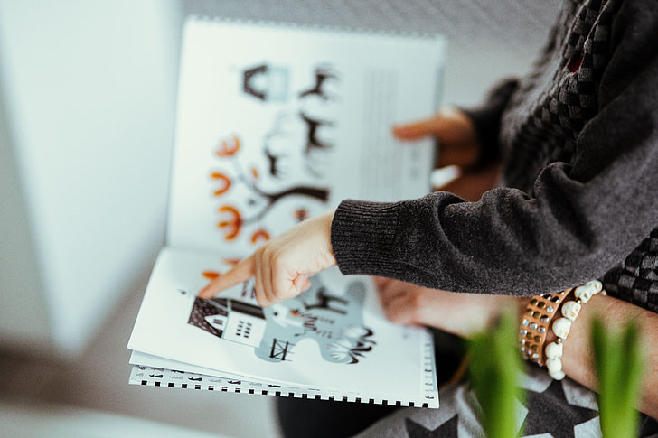 Criança e adulto apontando ilustrações em um livro. Imagem ilustrativa texto campo artístico-literário. 