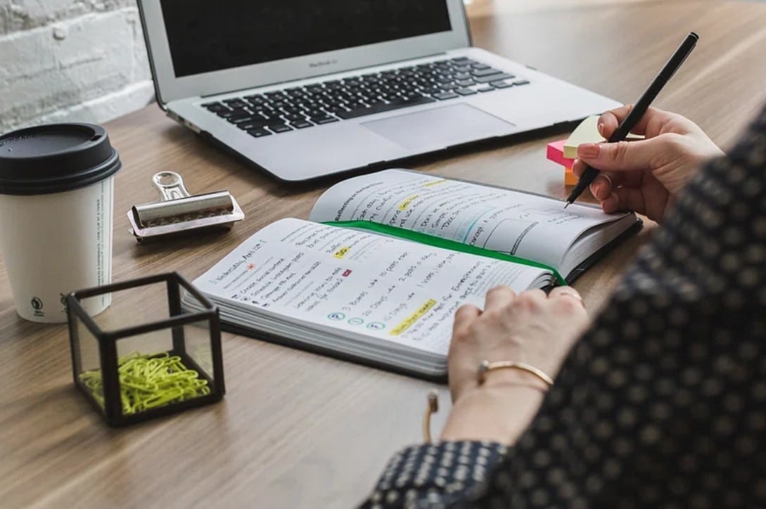 Mulher escrevendo anotações em frente ao computador. Imagem ilustrativa texto carreira de escritor.
