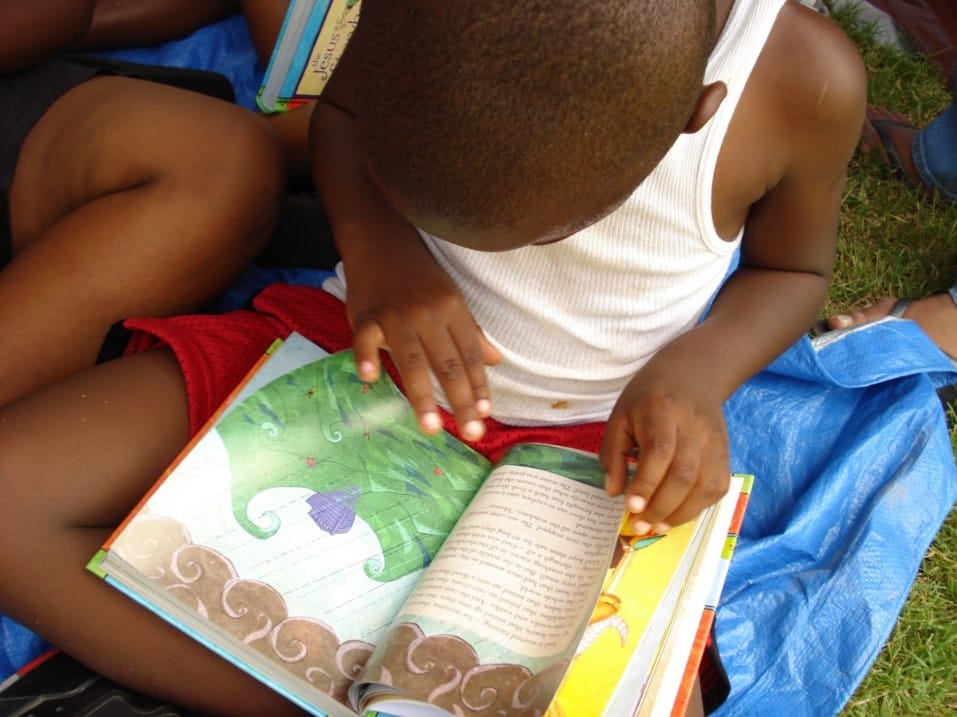 Menino com livro no colo, lendo. Imagem ilustrativa texto brincadeiras para incentivar leitura.